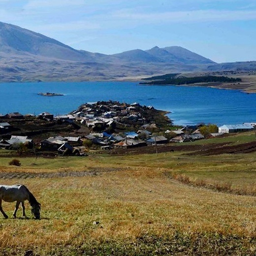 Белая лошадь пасется на фоне горного озера Табацкури и старинного поселения